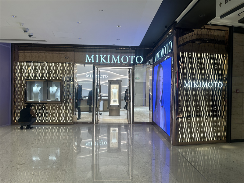 The illuminated storefront combines patterned metal screens, brand signage, a jewelry window display, and a digital campaign panel to create a distinctive entrance presentation.