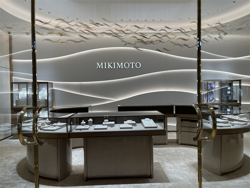 A wave-inspired illuminated wall and suspended decorative elements create a refined backdrop for the central jewelry display area.