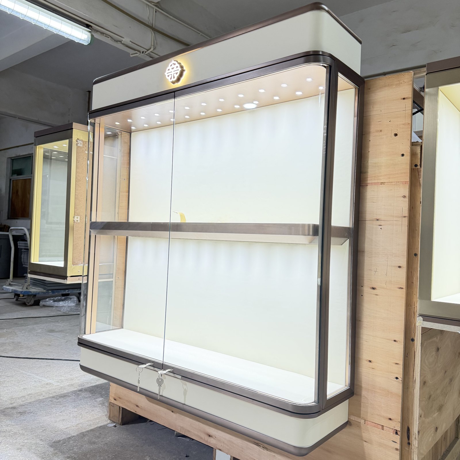 Long glass jewelry display counter with enclosed lower cabinets and illuminated base in a workshop
