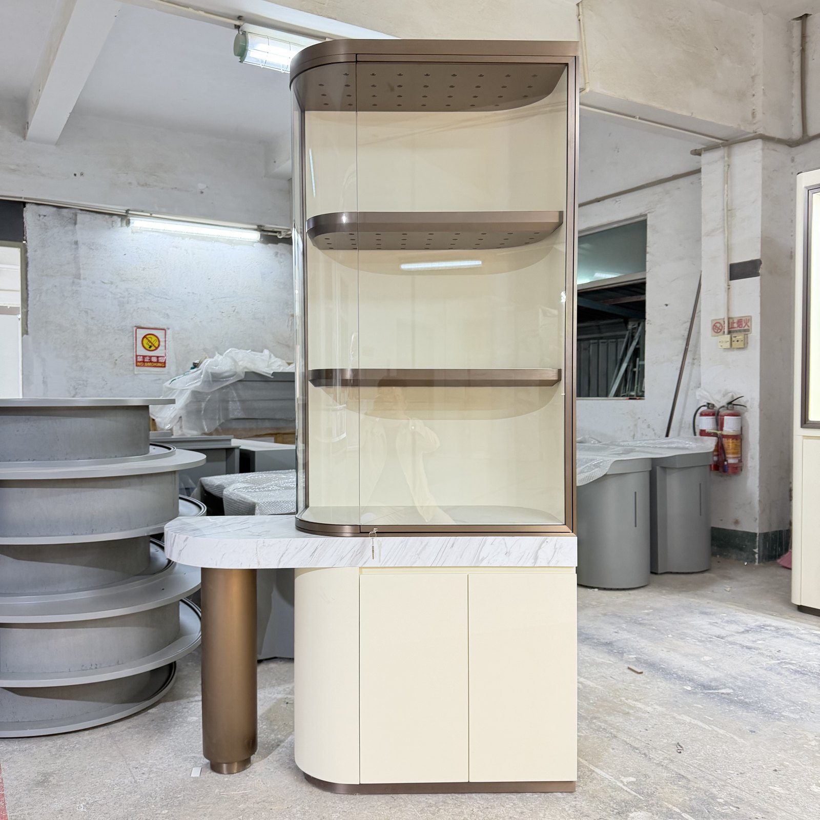 Rounded jewelry display cabinet with a projecting side surface and lower storage doors in a workshop