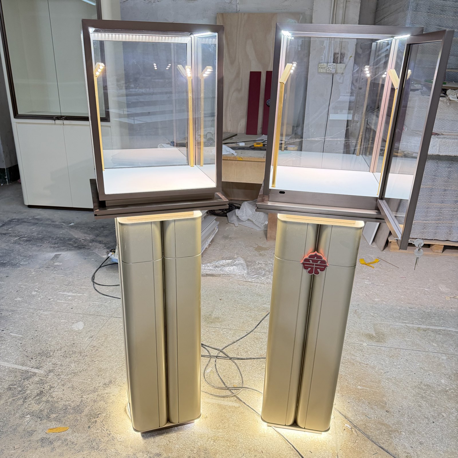 Two illuminated pedestal jewelry showcases with narrow metallic bases in a workshop