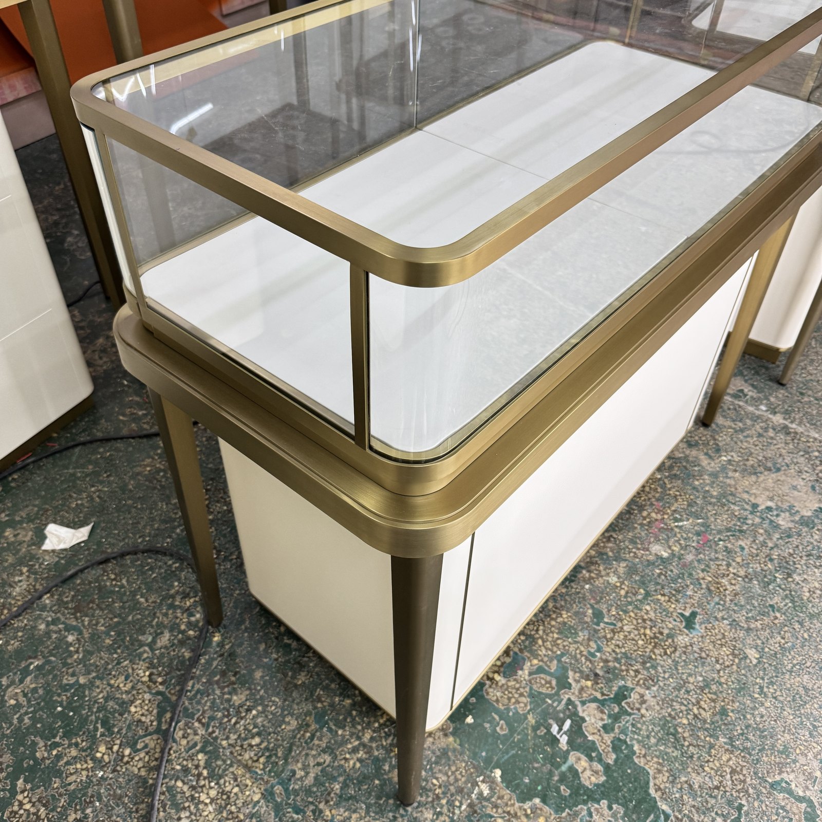 Jewelry island counter with a gold-toned metal frame and white cabinet base