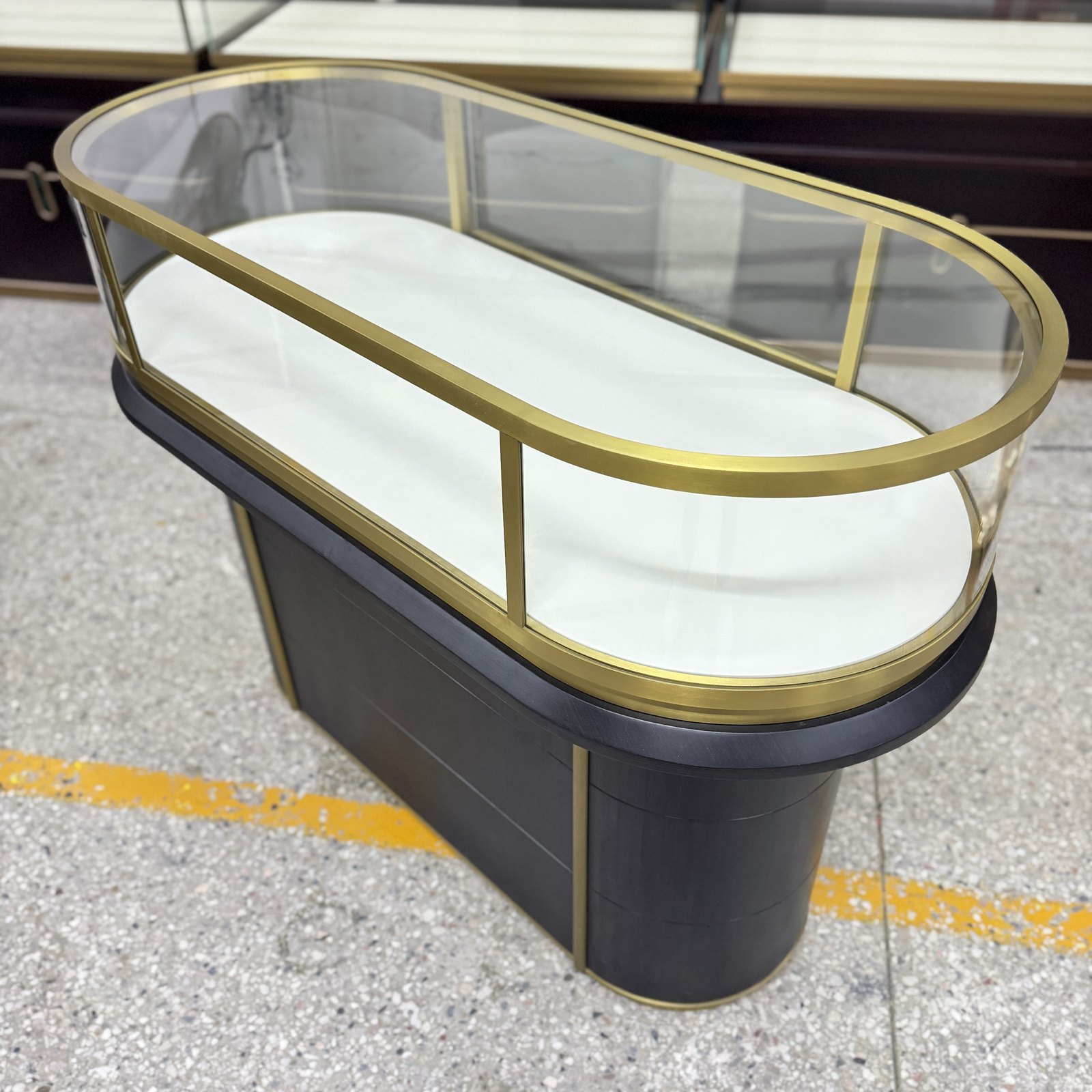Oval jewelry pedestal showcase with a gold-toned metal rail and enclosed base