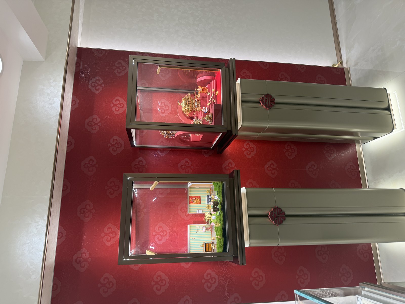 Two pedestal jewelry showcases displaying jewelry against a red decorative wall inside the store