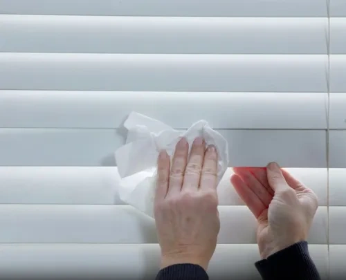 Hand holding paper towel to wipe wooden blinds