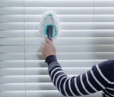 Hand holding brush to clean wooden blinds